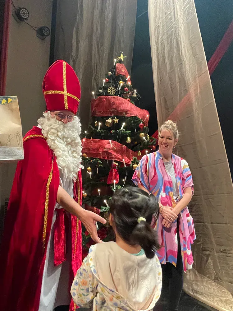 A man dressed as santa claus is shaking hands with a little girl in front of a christmas tree.