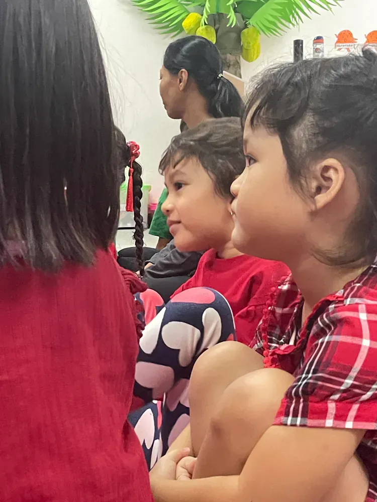 A group of children are sitting on the floor looking at something.