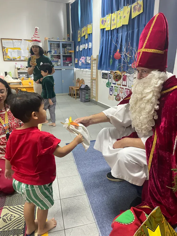 A little boy is giving a gift to a man dressed as santa claus.