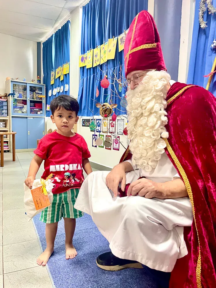 A man dressed as santa claus is kneeling down next to a little boy.