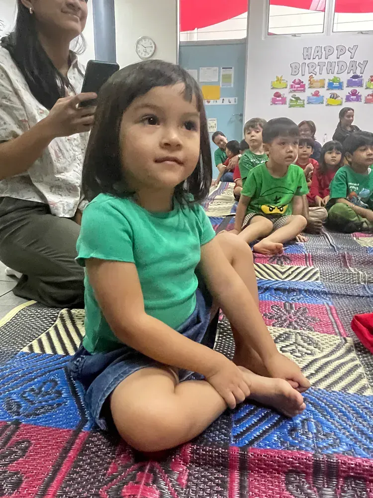 A little girl is sitting on the floor in front of a group of children.