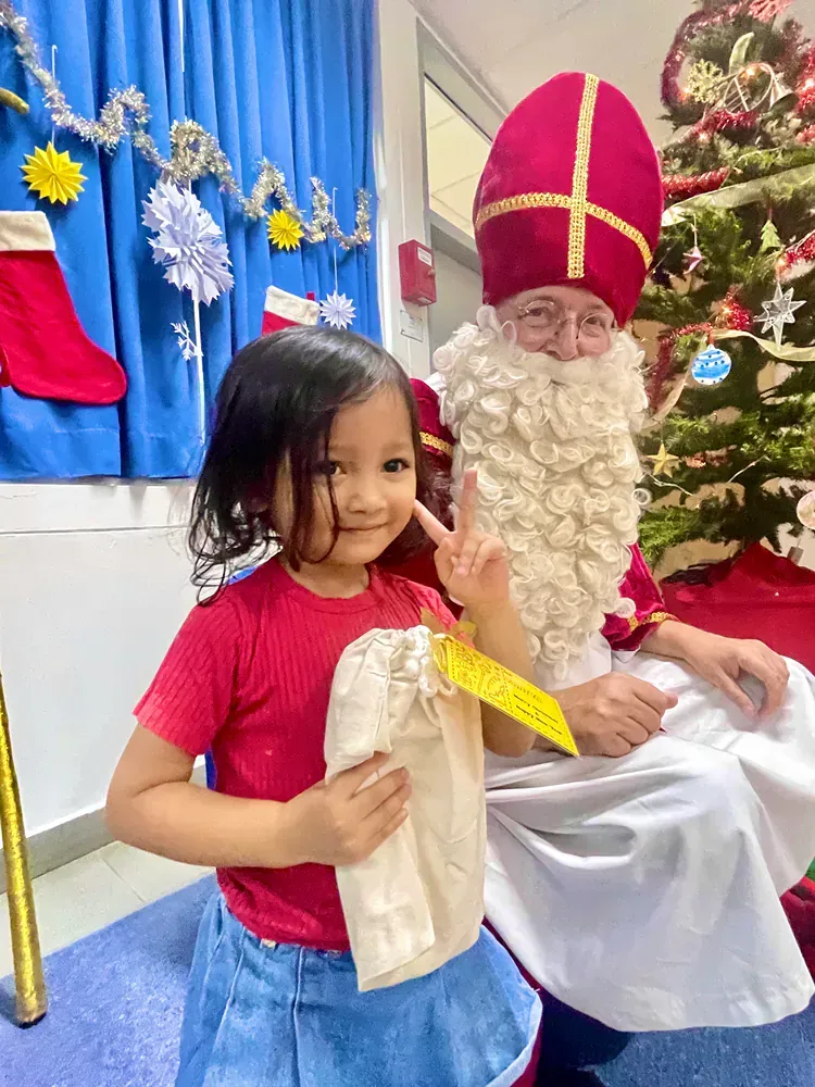 A little girl is sitting next to a man dressed as santa claus.