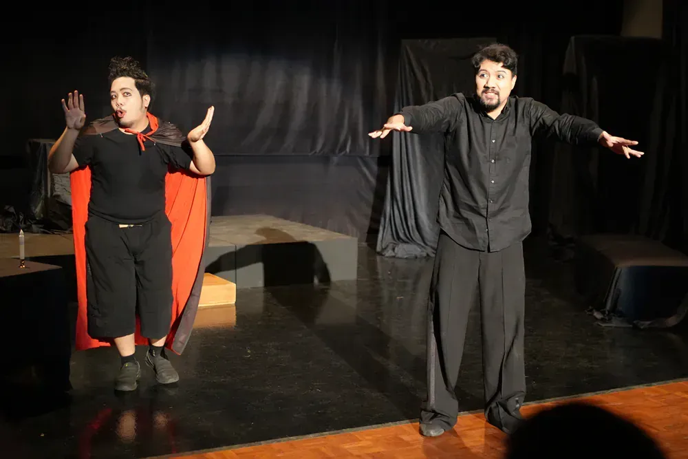 Two men are standing on a stage with their arms outstretched.