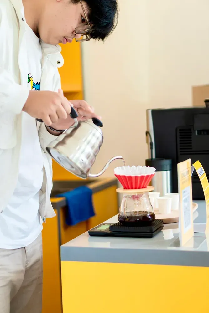 A man is pouring coffee from a kettle into a cup.