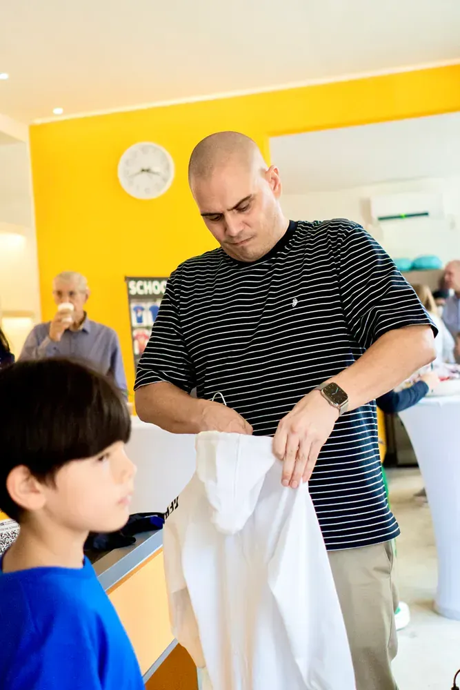 A man in a striped shirt is holding a white shirt in front of a boy in a blue shirt.