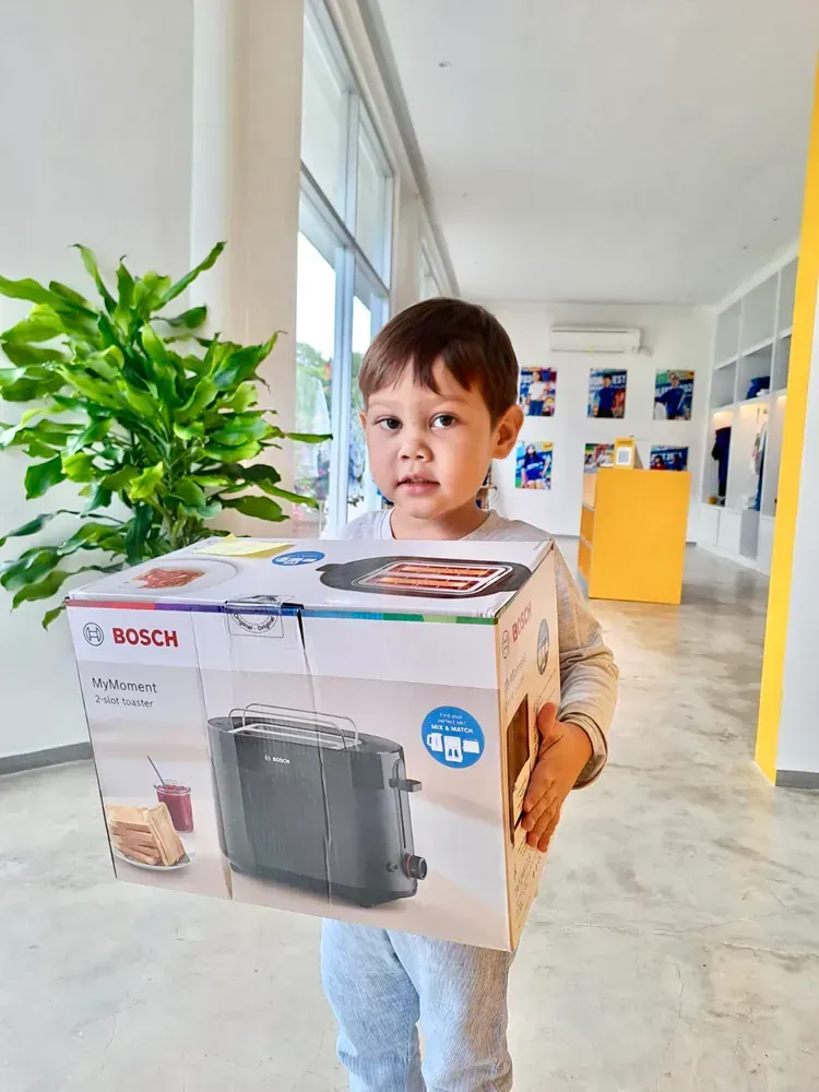A little boy is holding a box of a toaster.