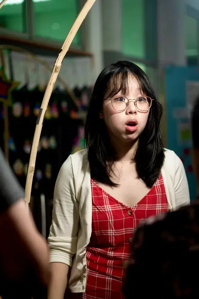 A young woman wearing glasses and a red dress is holding a stick in her hand.