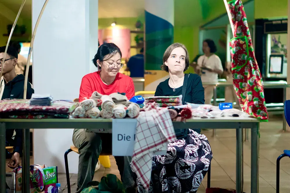 Two women are sitting at a table with a sign that says die