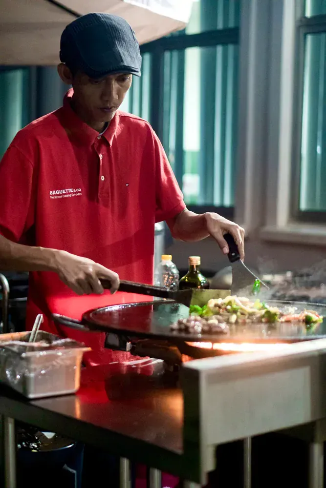 A man in a red shirt is cooking food on a grill.