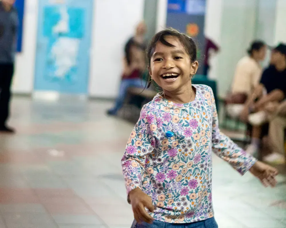 A little girl is standing in a hallway and smiling.