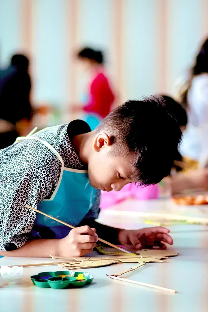 A young boy is laying on the floor painting a picture.
