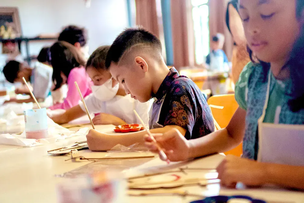 A group of children are sitting at a table painting.