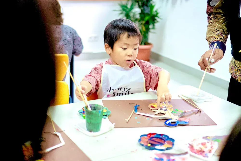 A young boy is sitting at a table painting with a brush.