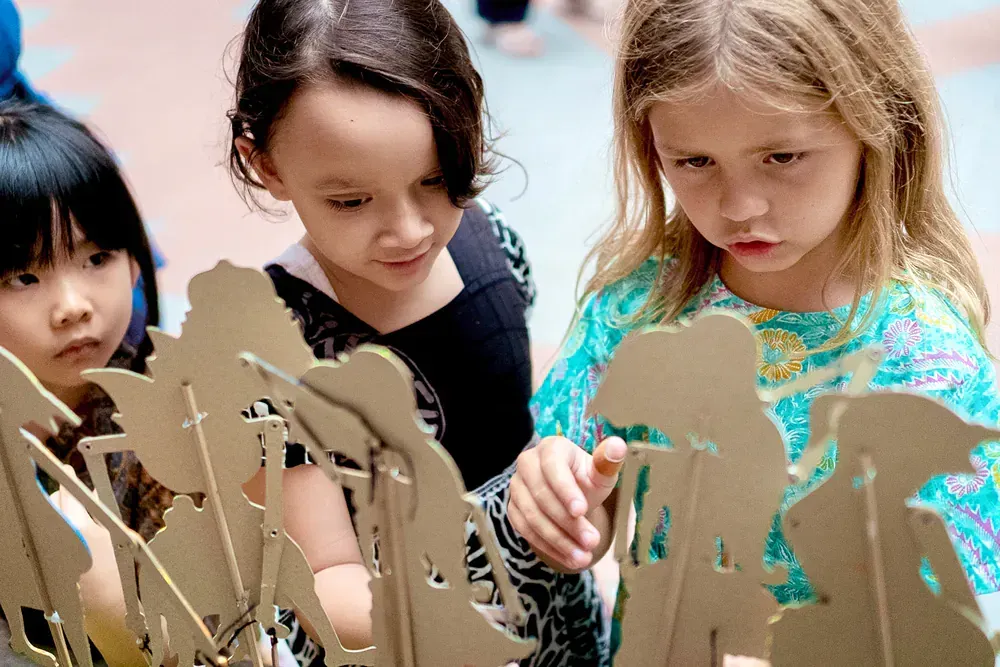 Three young girls are looking at a cardboard sculpture.