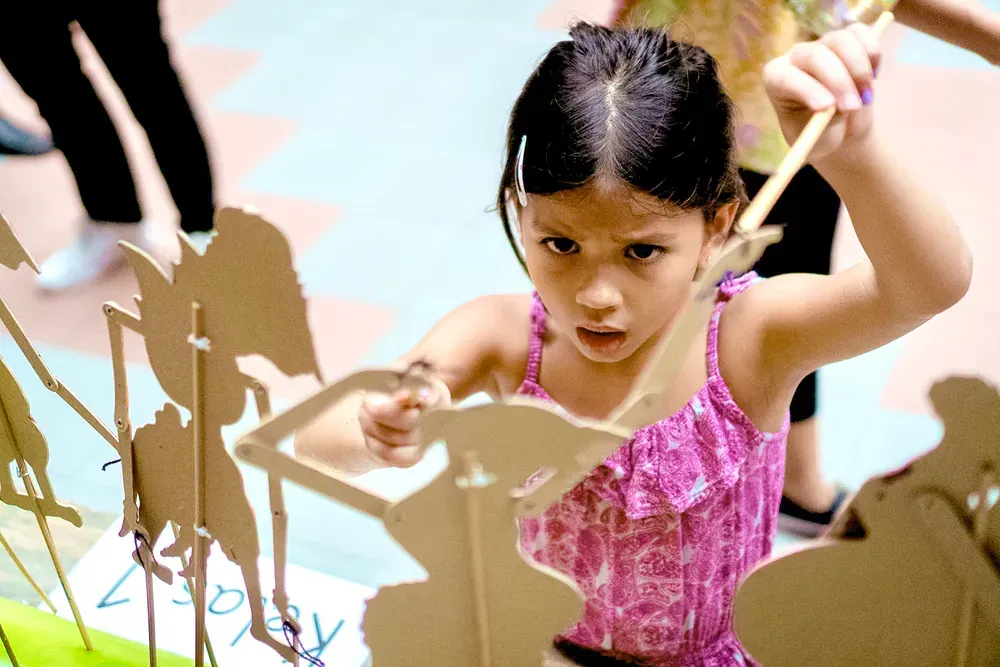 A little girl in a pink dress is playing with cardboard animals