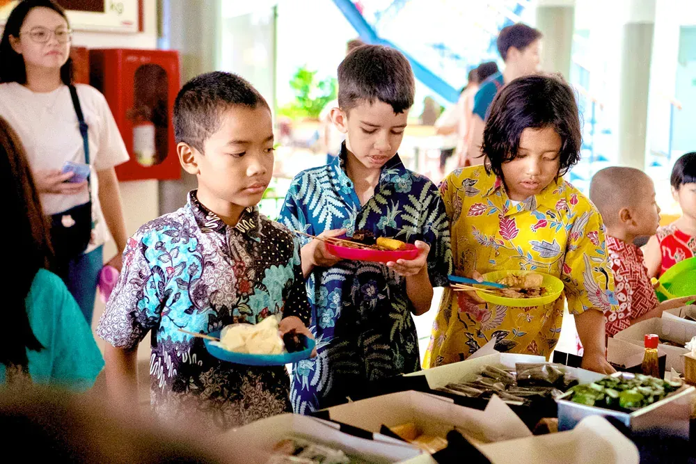 A group of children are standing around a table eating food.