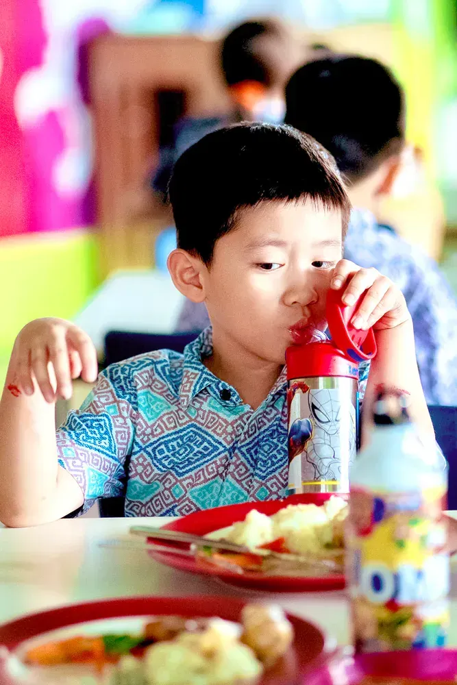 A young boy is sitting at a table drinking from a bottle.