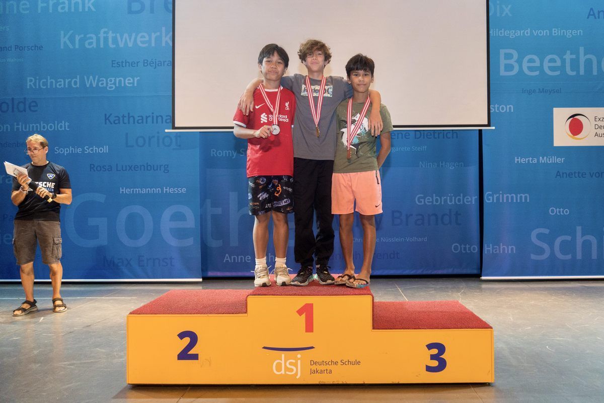 Three boys are standing on a podium with the number 1 on it