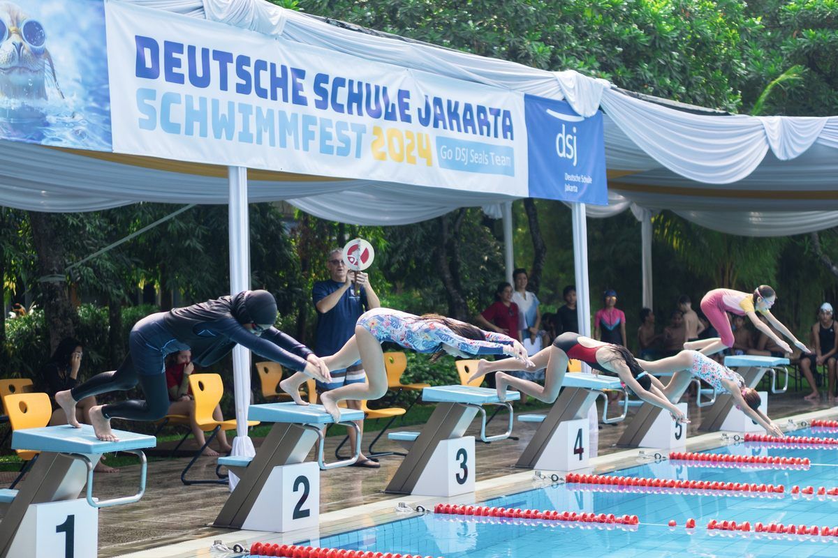 A group of people are swimming in a pool under a sign that says deutsche schule jakarta