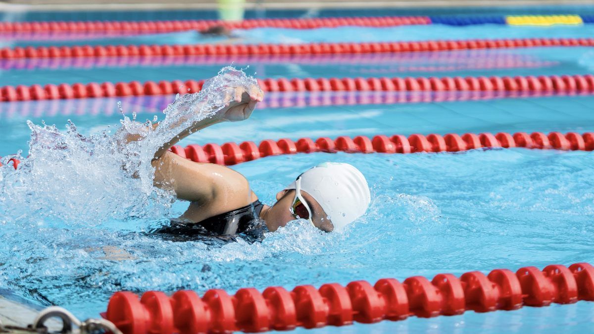 A person is swimming in a swimming pool with red lanes.