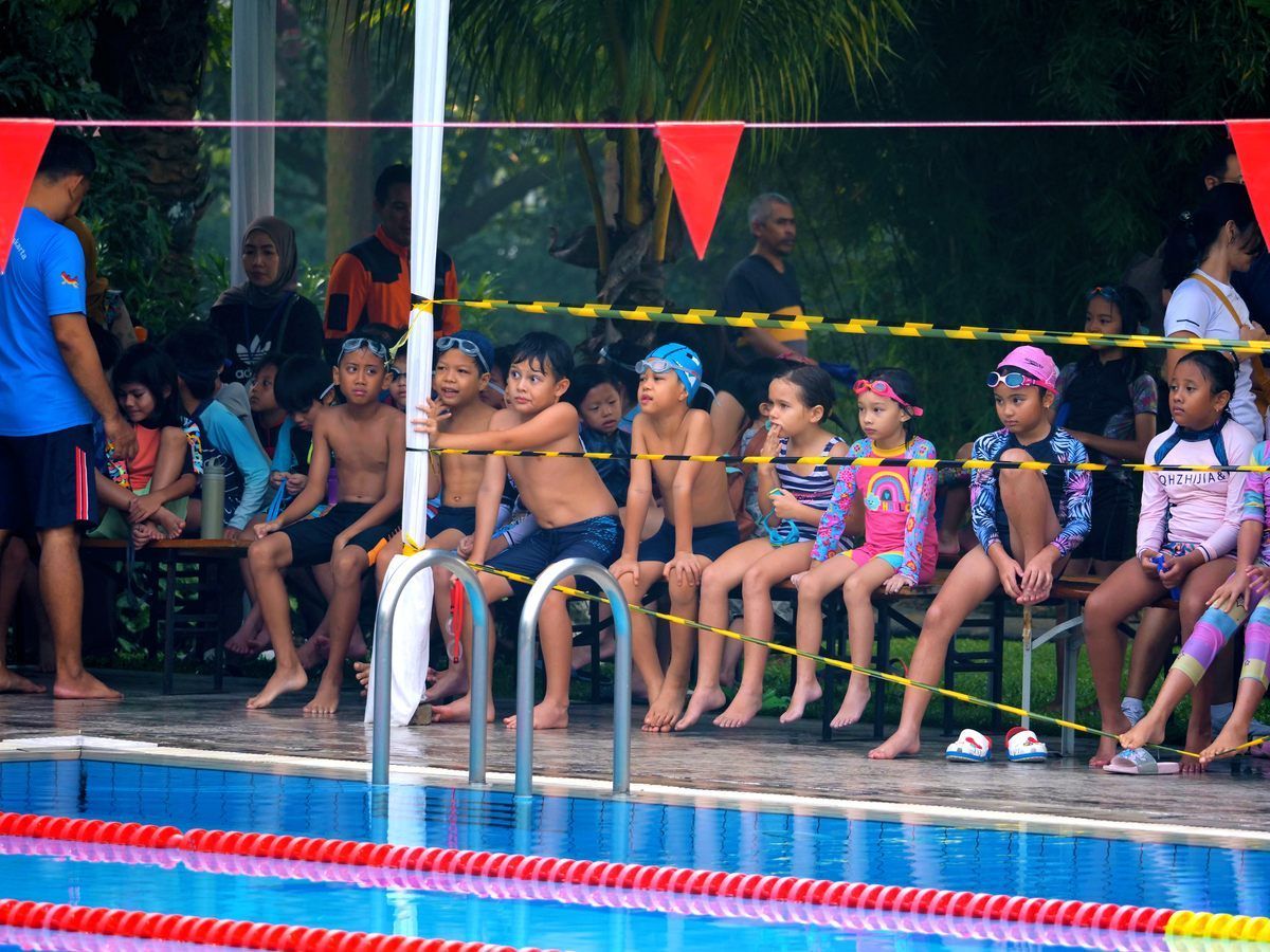 A group of children are sitting on a bench near a swimming pool.