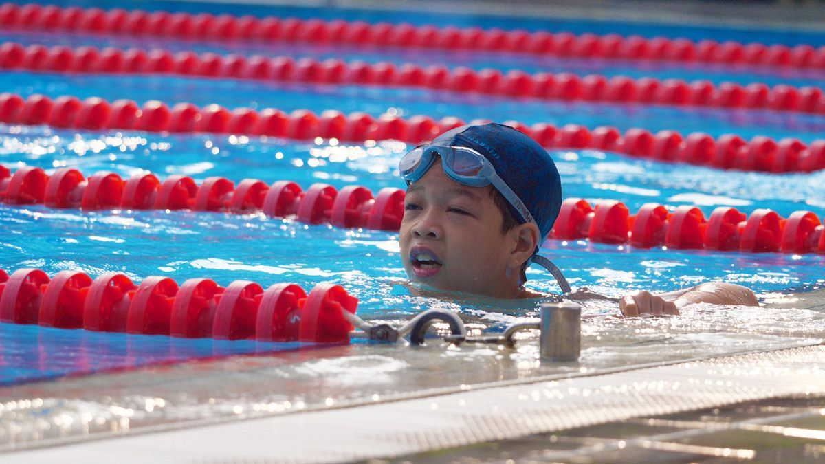 A young boy is swimming in a pool with red lanes.