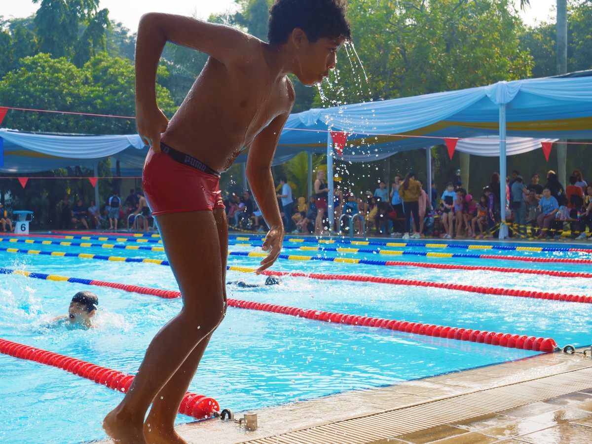 A young boy in red swim trunks stands at the edge of a swimming pool