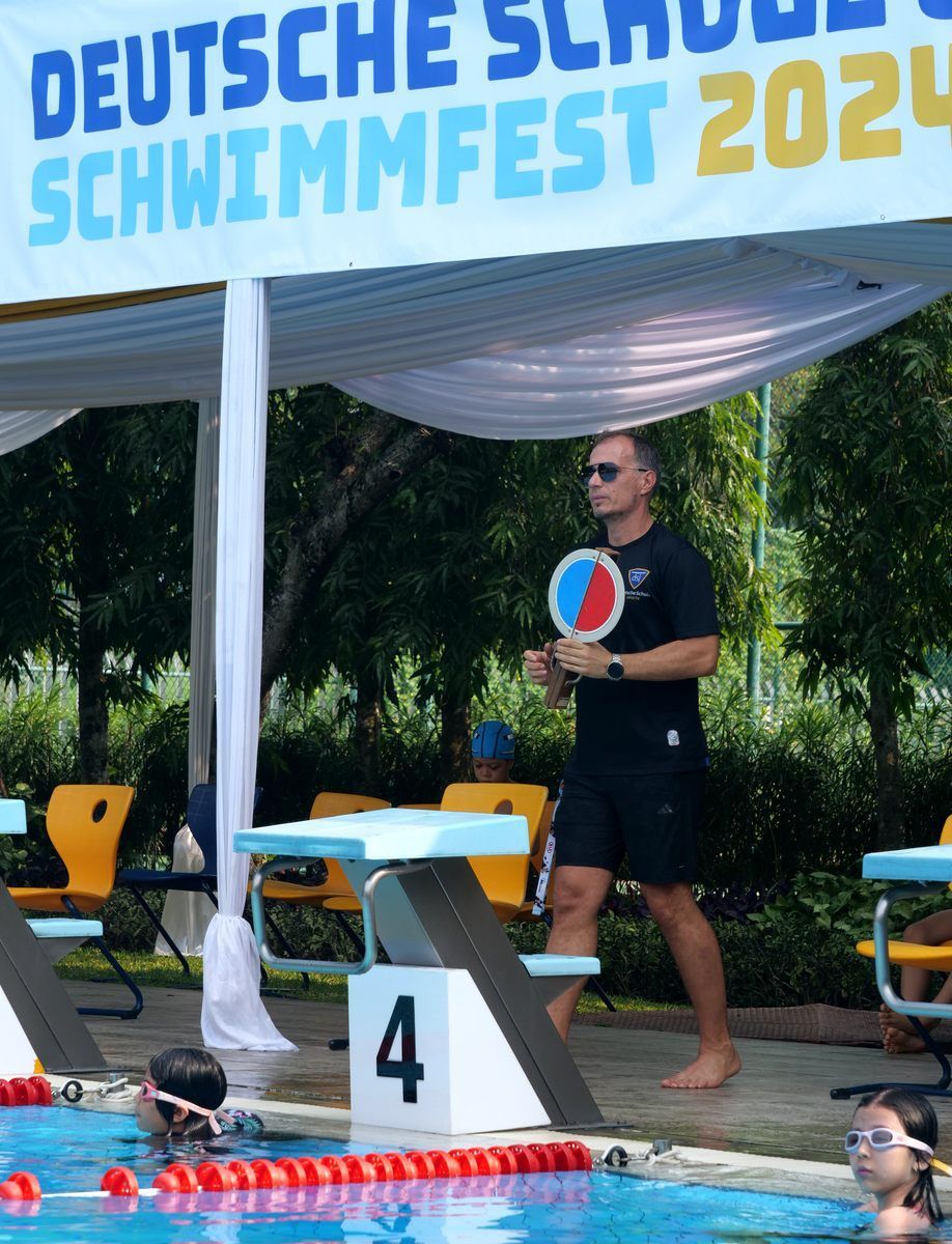 A man stands in front of a sign that says deutsche schwimmfest