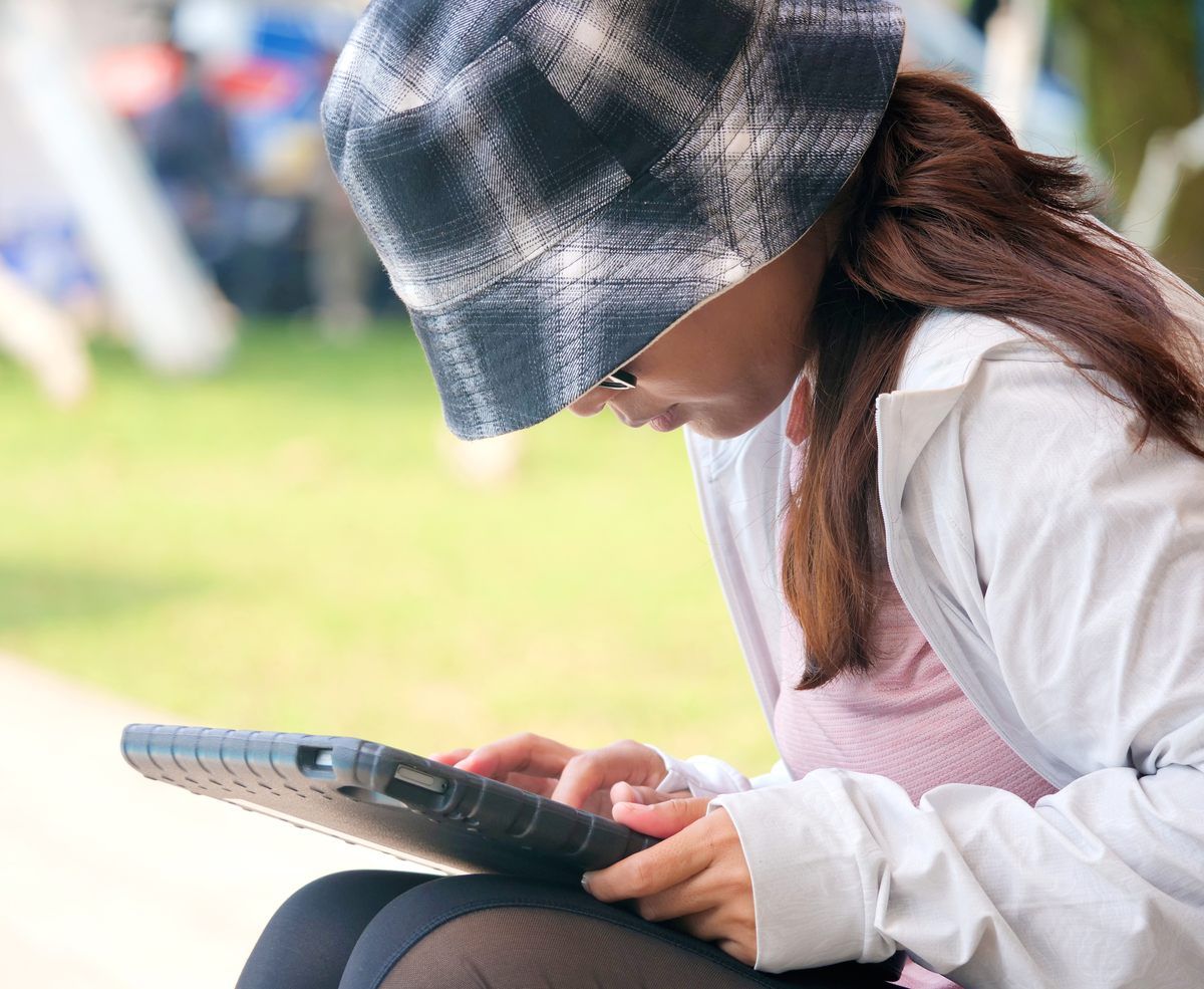 A woman wearing a plaid hat is using a tablet