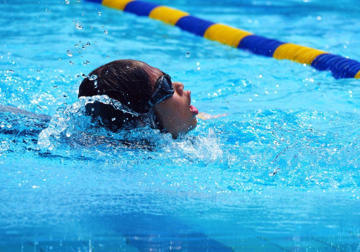 A person wearing goggles is swimming in a pool.