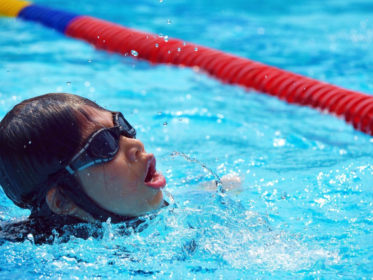 A young girl wearing goggles is swimming in a pool.
