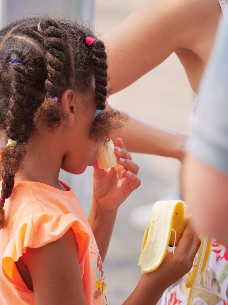 A little girl is eating a slice of banana