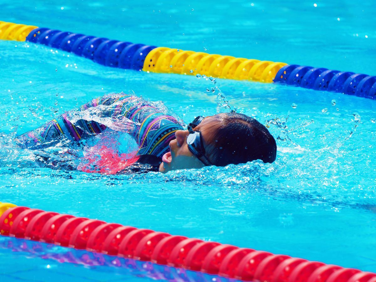 A person is swimming in a pool wearing goggles.