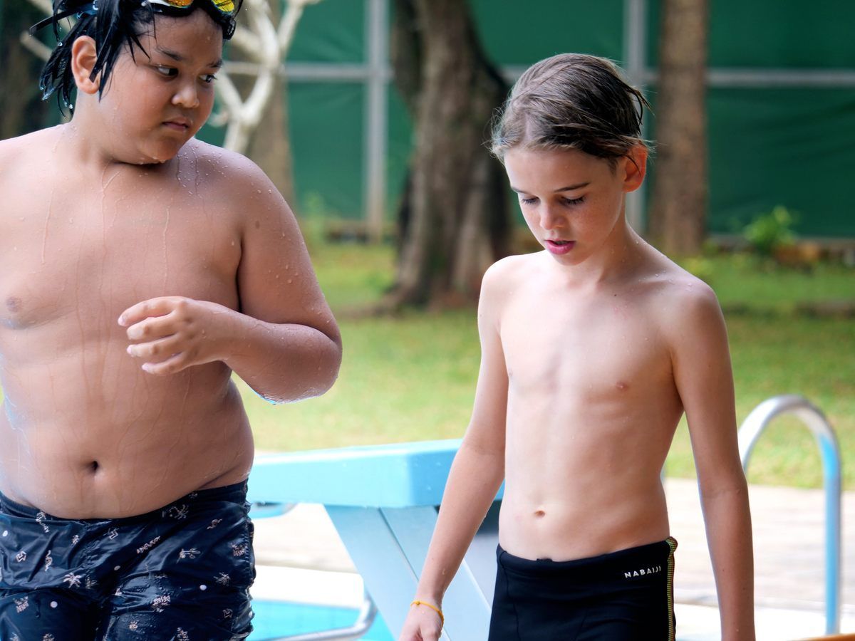 Two boys in swim trunks walk near the poolside, engaged in conversation.