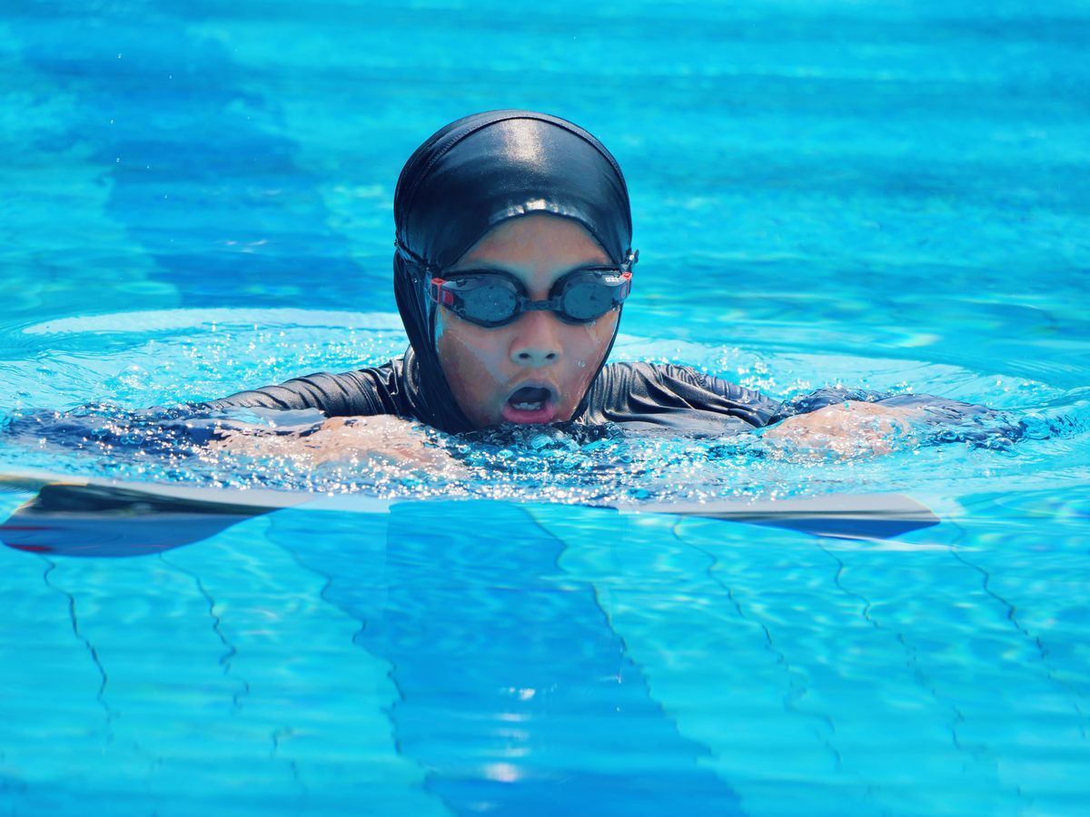 A woman is swimming in a pool wearing a hijab and goggles.