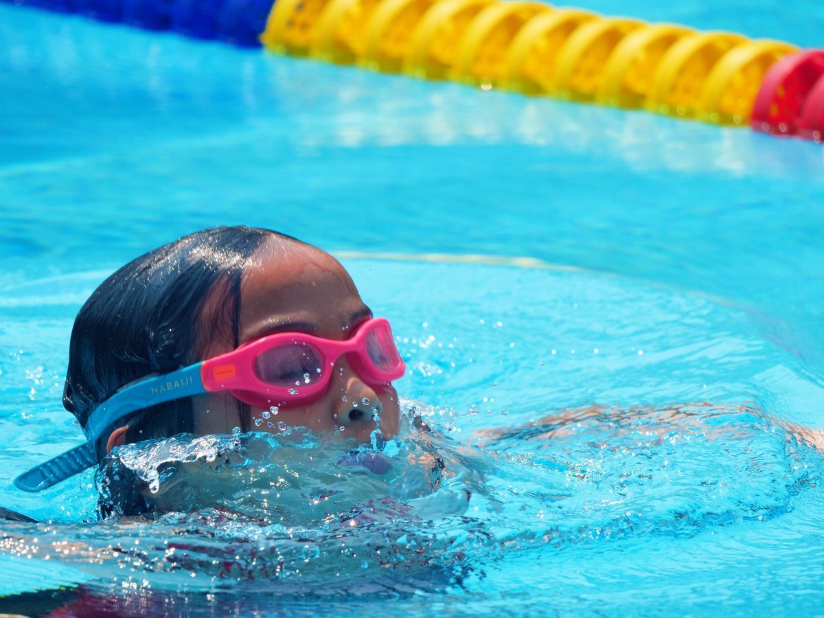 A young girl wearing pink goggles is swimming in a pool.