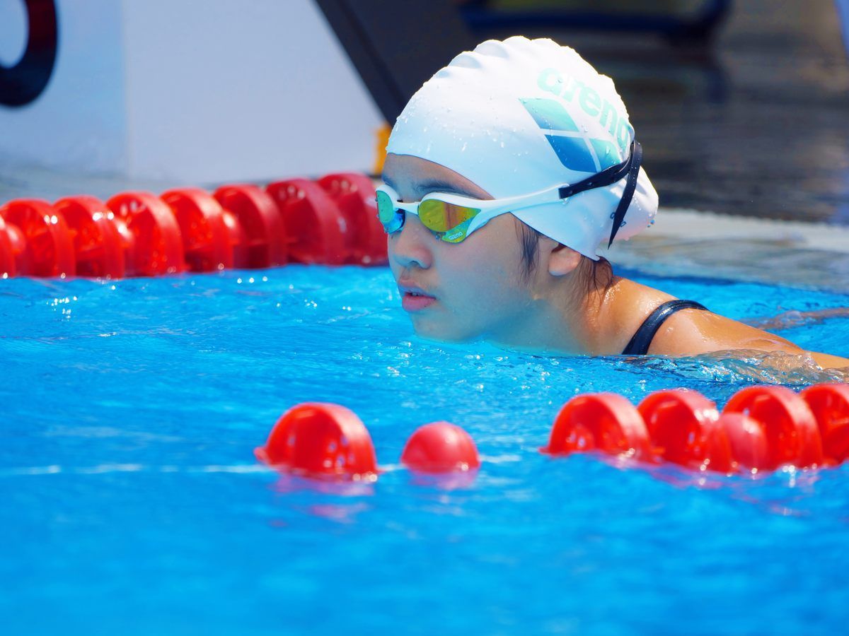 A woman wearing a swim cap and goggles is swimming in a pool.