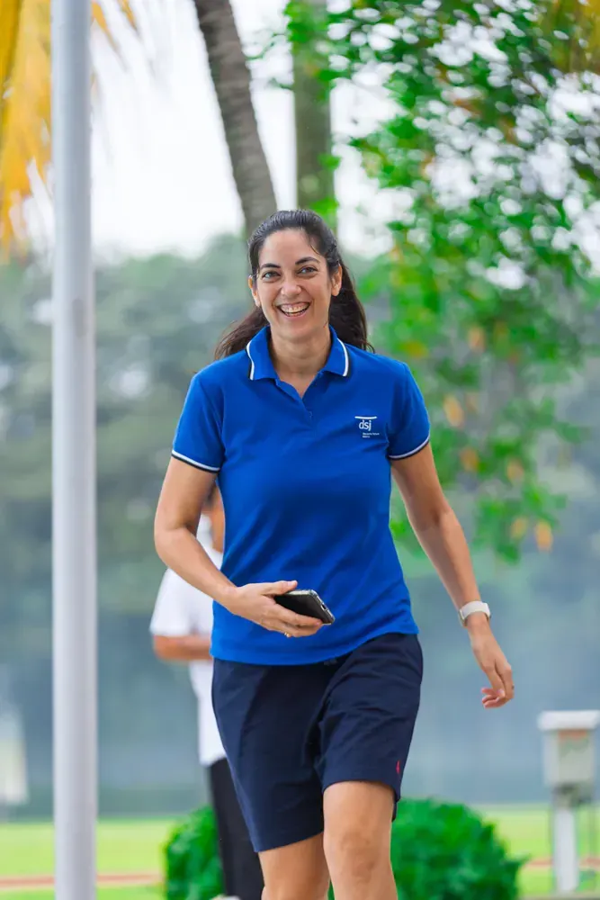 A woman in a blue shirt and shorts is walking down a sidewalk while holding a cell phone.