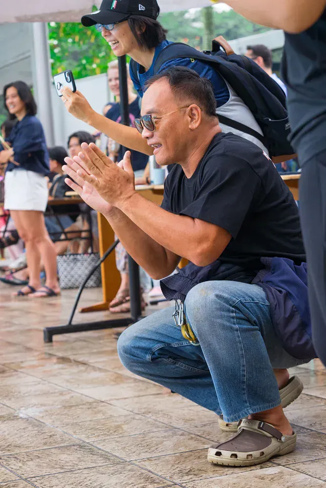 A man is squatting down while a woman takes a picture of him.