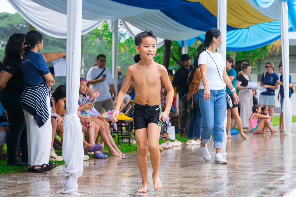 A young boy without a shirt is walking in the rain.