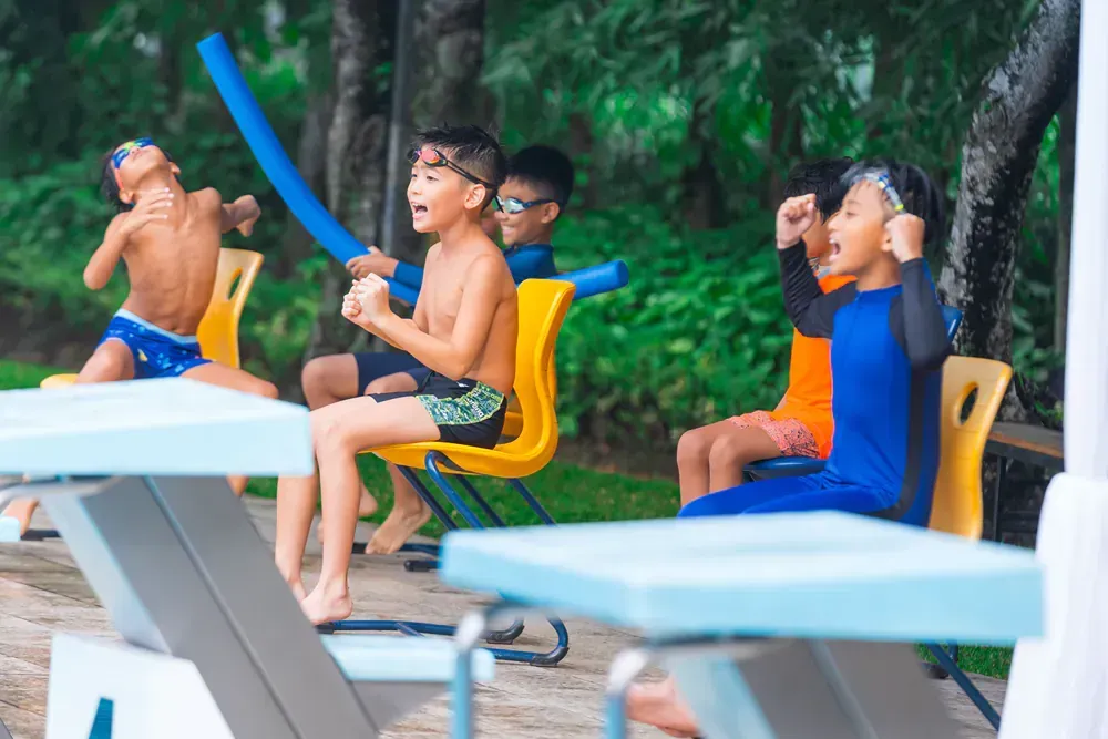 A group of young boys are sitting on chairs in front of a swimming pool.
