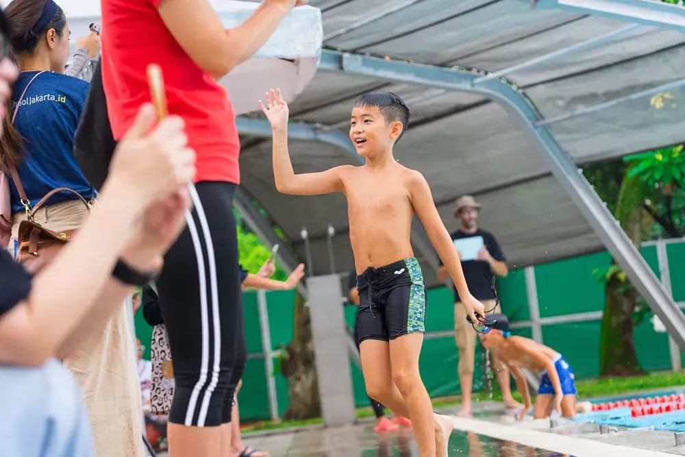 A happy child near a swimming pool in a group of people waving.