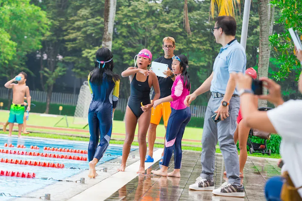 A group of children are standing next to a swimming pool.