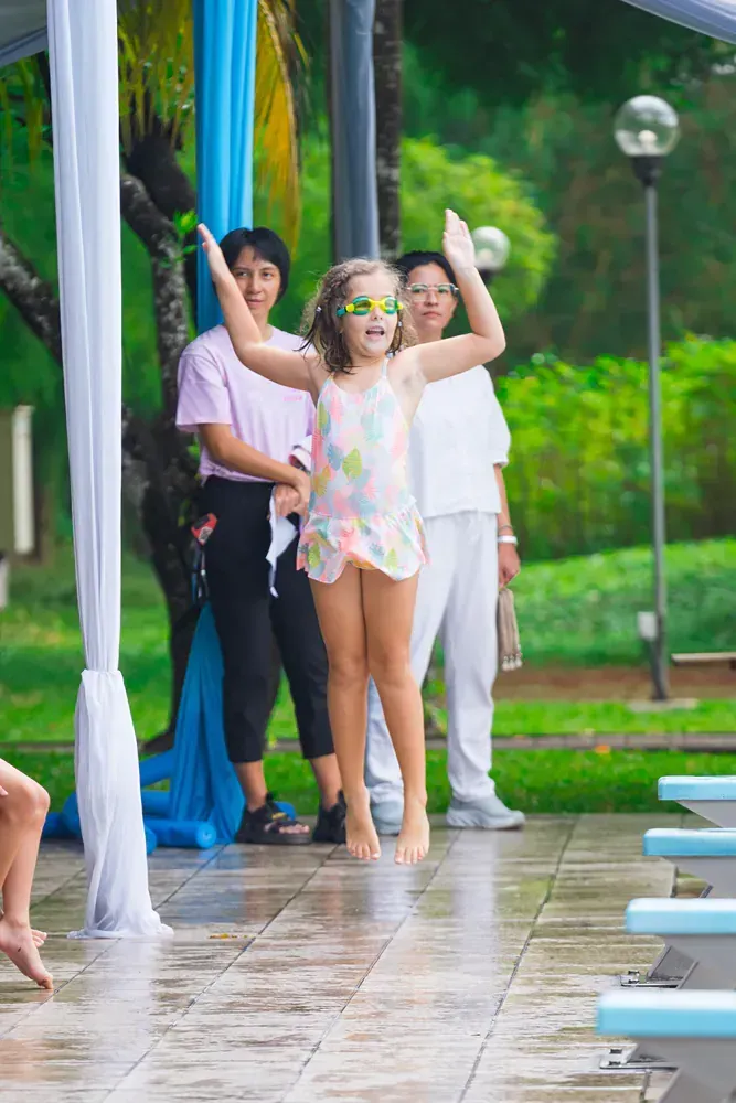 A little girl is wearing sunglasses and dancing in front of a pool.