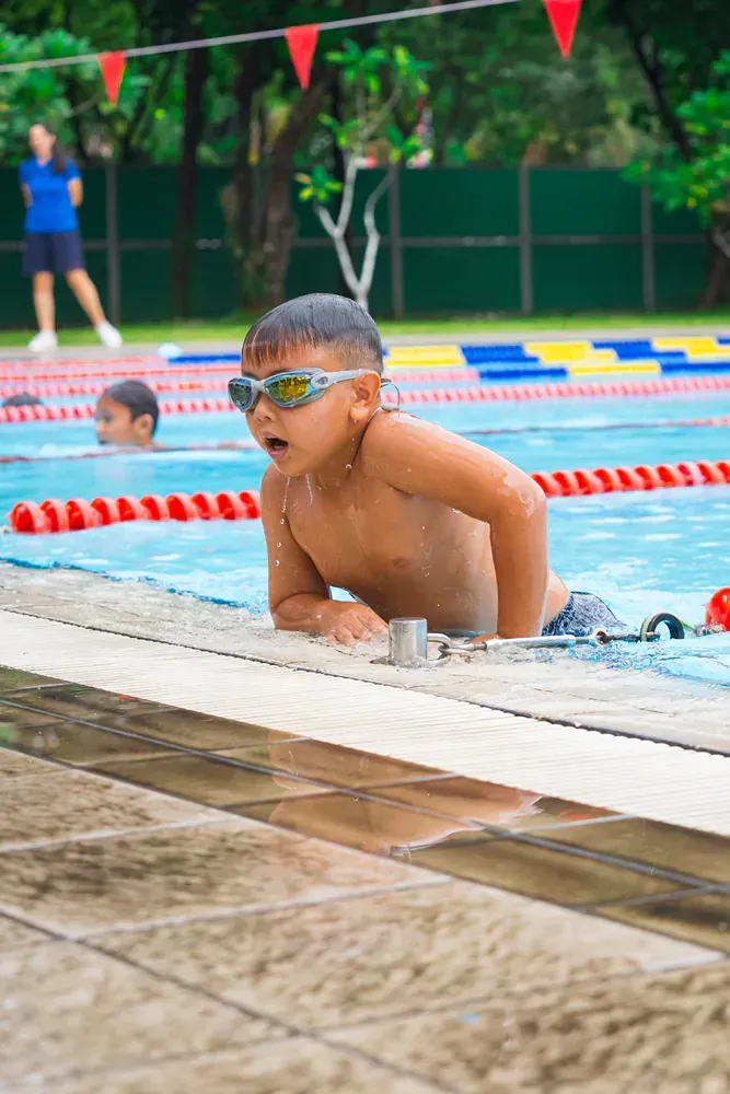 A young boy wearing goggles is swimming in a swimming pool.