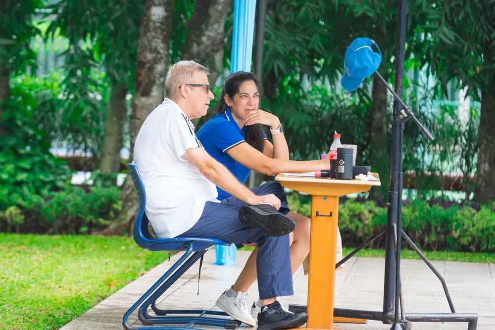 A man and a woman are sitting at a table in a park.