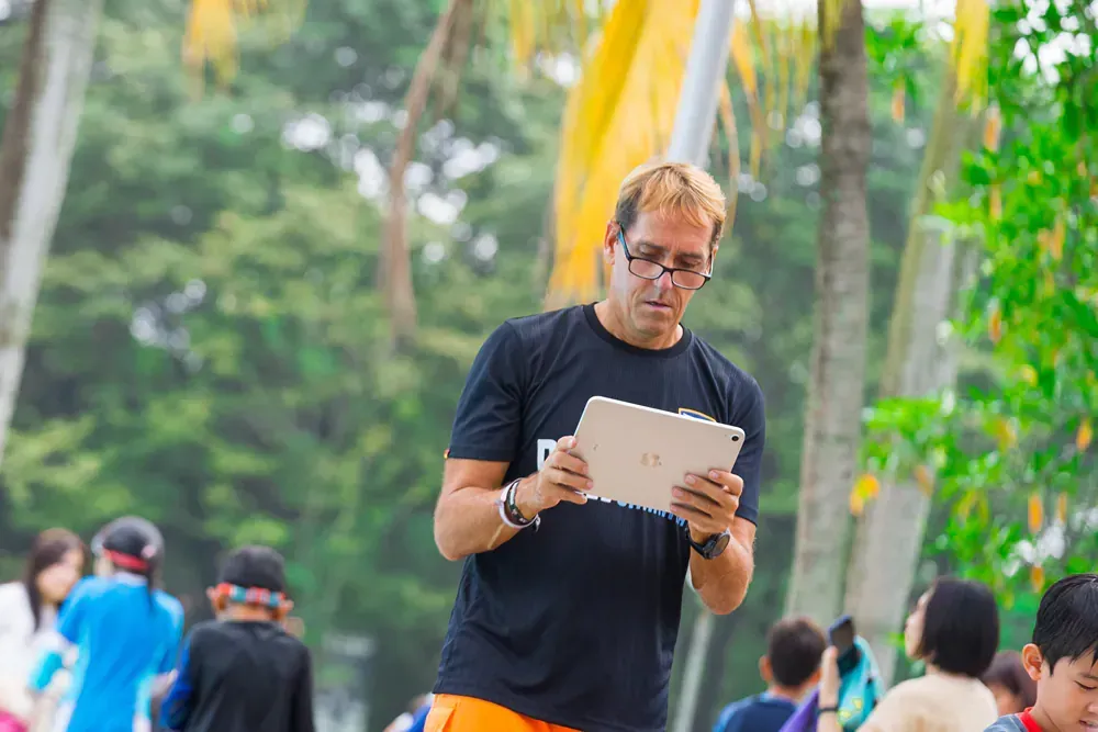 A man is standing in a park looking at a tablet.