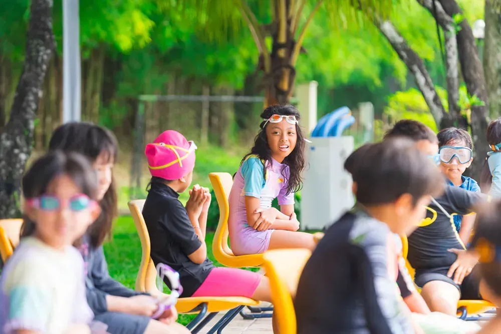 A group of children are sitting on chairs in a park.