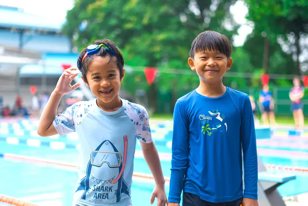 A boy and a girl are standing next to each other in front of a swimming pool.