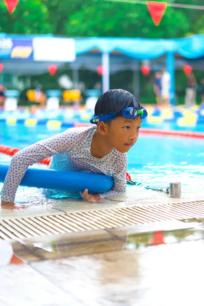 A young boy is sitting on a blue float in a swimming pool.